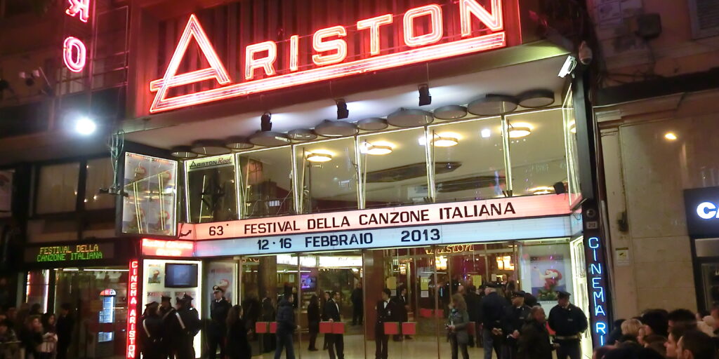 Aufnahme des Ariston-Theaters in Sanremo an einem Abende des Festivals 2013. Zuschauer sind außerhalb der Absperrungen zu sehen, während sich im Eingangsbereich Sicherheitskräfte aufhalten.