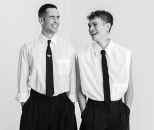 Schwarzweiß-Foto von Mahmood & Blanco, die dunkle Hosen und weiße Hemden mit dunklen Krawatten tragen.