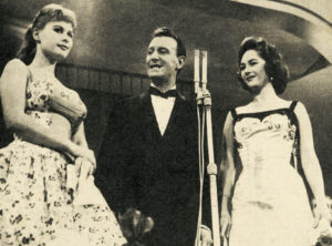 Schwarz-Weiß-Foto von Marisa Allasio, Nunzio Filogamo und Fiorella Mari vor einem Standmikrofon auf der Bühne des Sanremo-Festivals 1957.