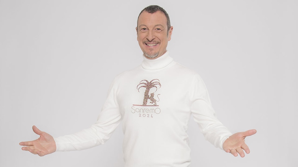 Amadeus steht mit ausgebreiteten Armen vor einem weißen Hintergrund. Er trägt einen weißen Pullover, auf dem die typische Palme und der Löwe von Sanremo sowie der Schriftzug „Sanremo 2024“ zu sehen sind.