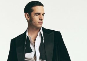 Achille Lauro mit offenem Hemd und schwarzer Anzugjacke, er blickt seitlich nach unten