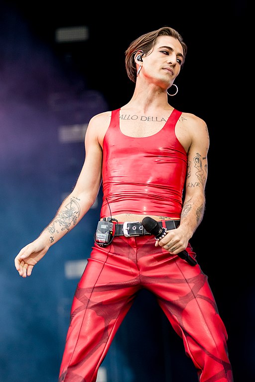 Damiano David in rotem Outfit hält ein Mikrofon in der linken Hand und blickt zur Seite