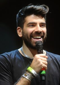 Gianluca Gazzoli spricht in ein Handmikrofon; er trägt ein dunkles T-Shirt