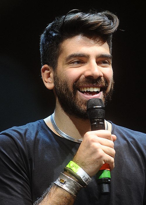 Gianluca Gazzoli spricht in ein Handmikrofon; er trägt ein dunkles T-Shirt