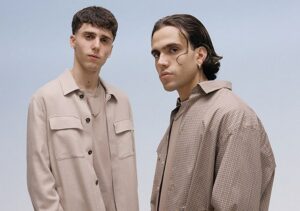 LDA und Aka 7even stehen nebeneinander vor einem neutralen Hintergrund. Beide blicken direkt in die Kamera. Das Porträt wirkt professionell ausgeleuchtet und zeigt die beiden Künstler in halbnaher Einstellung.