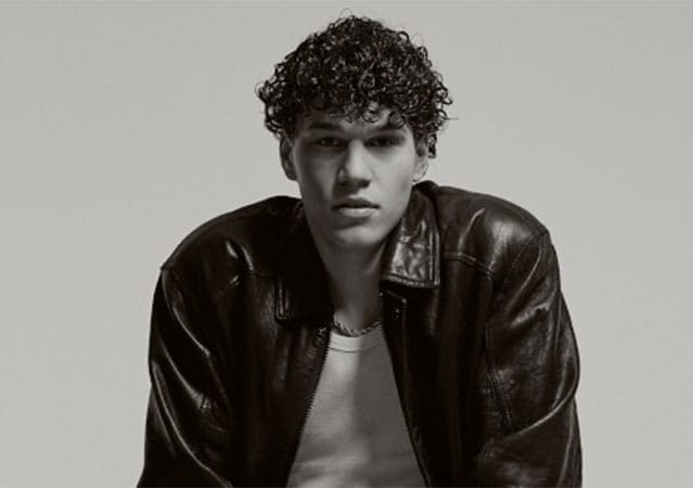 Schwarz‑Weiß-Porträt Nicolò Filippuccis mit lockigem Haar, der eine dunkle Lederjacke über einem hellen Shirt trägt. Er befindet sich vor einem schlichten Hintergrund und blickt ruhig und direkt in die Kamera; Licht und Kontraste betonen die Texturen von Haar und Jacke.