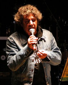 Nahaufnahme des Sängers Fausto Leali bei einem Konzert, mit leicht geneigtem Kopf, dunklem Hemd und neutralem Gesichtsausdruck vor unscharfem Hintergrund.