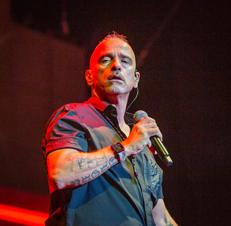 Eros Ramazzotti bei einem Auftritt im Oktober 2022. Er ist frontal im Bild zu sehen, trägt ein schwarzes T‑Shirt und hält ein Mikrofon in der rechten Hand. Sein Blick geht leicht zur Seite, der Hintergrund ist dunkel und lässt die Bühnenbeleuchtung dezent hervorscheinen. Das Foto wirkt wie eine Momentaufnahme während eines Live‑Konzerts.